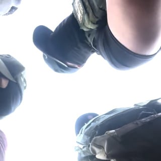 Agents stand over the camera; two wear masks over their entire faces.